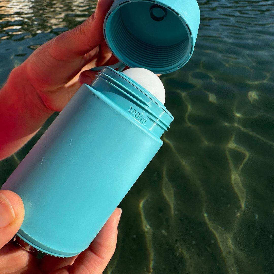 Blue refillable roll-on travel applicator held in hands with lid off