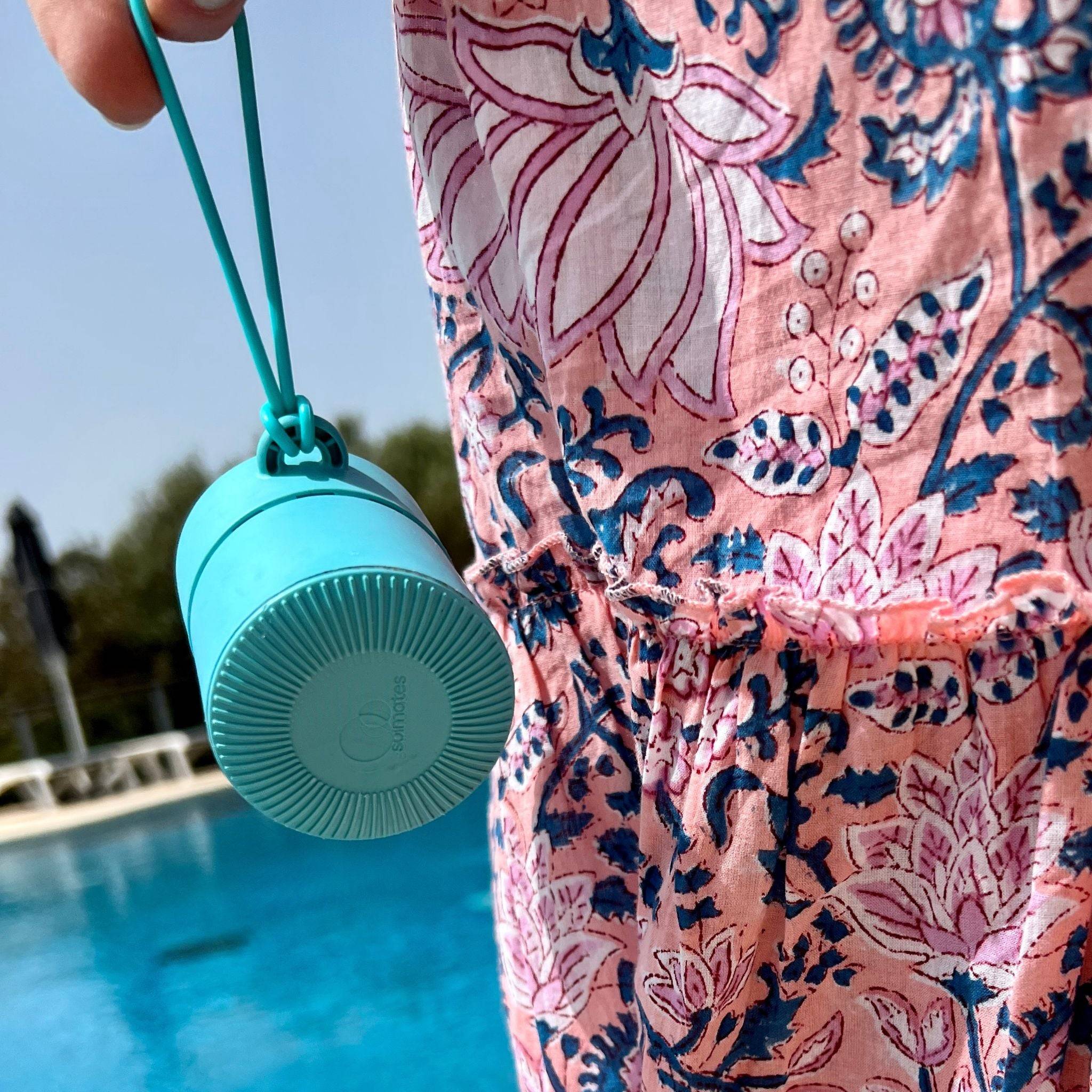 Blue refillable roll-on travel applicator held by the tether next to a long dress