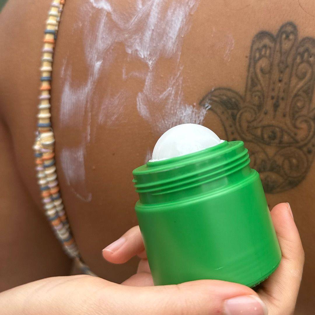 Green refillable roll-on travel applicator with lid off in front of a back covered in cream