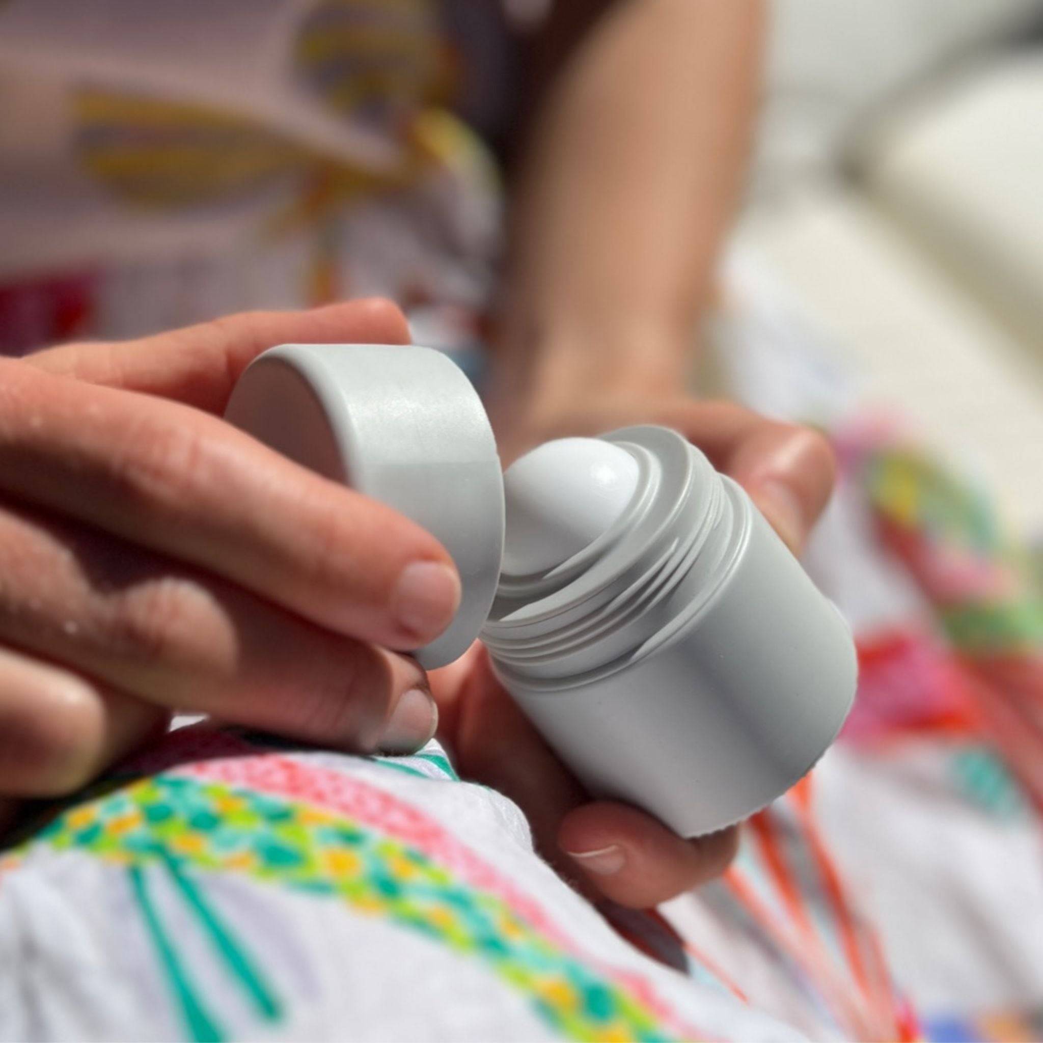 Grey refillable roll-on travel applicator held in hands in the lap of a woman