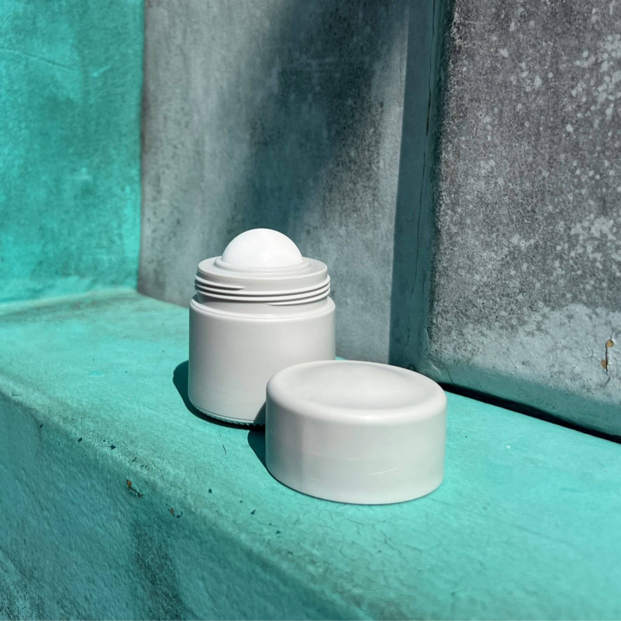 Grey refillable roll-on travel applicator with lid to the side on a green shelf
