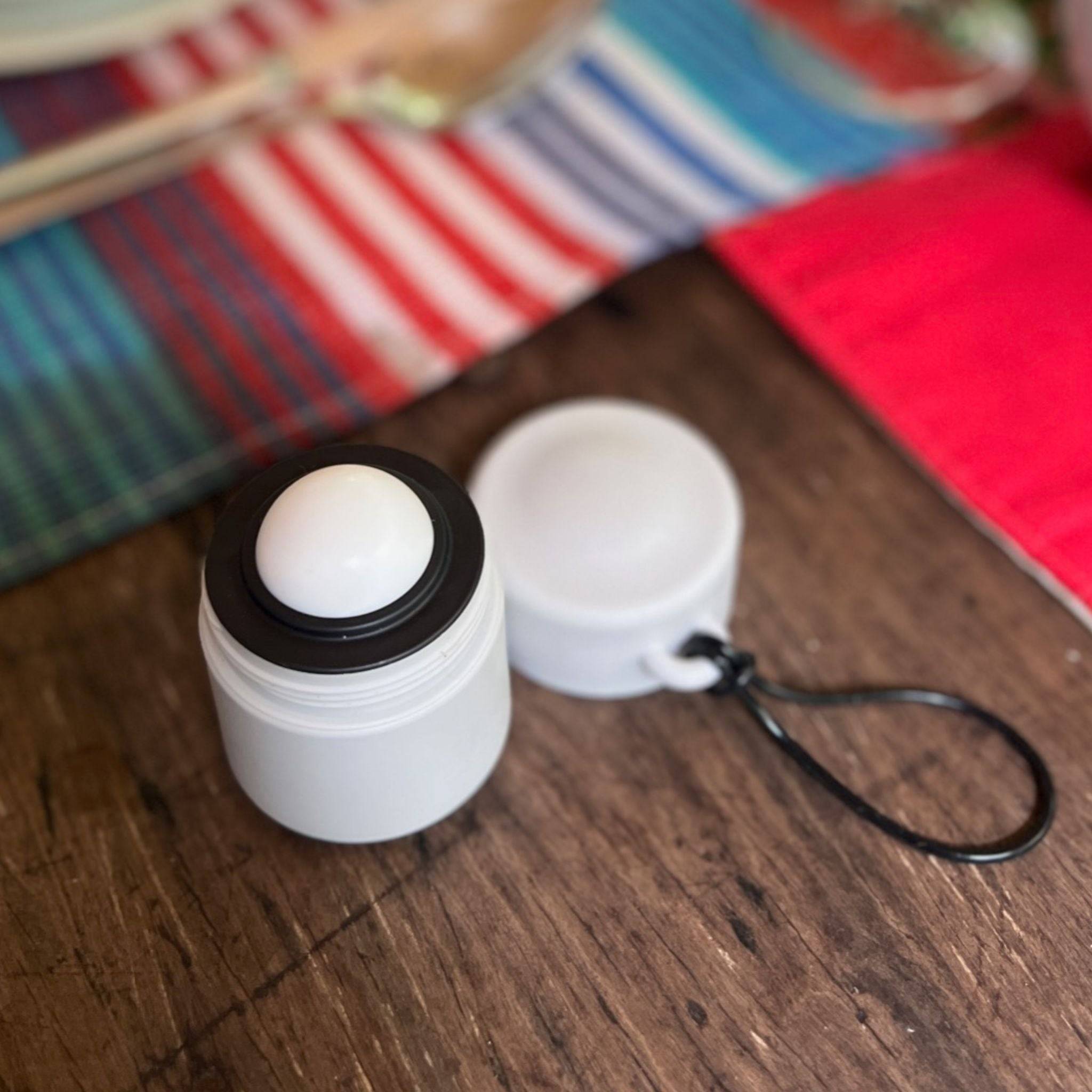 Grey and black refillable roll-on travel applicator with lid to the side on a table