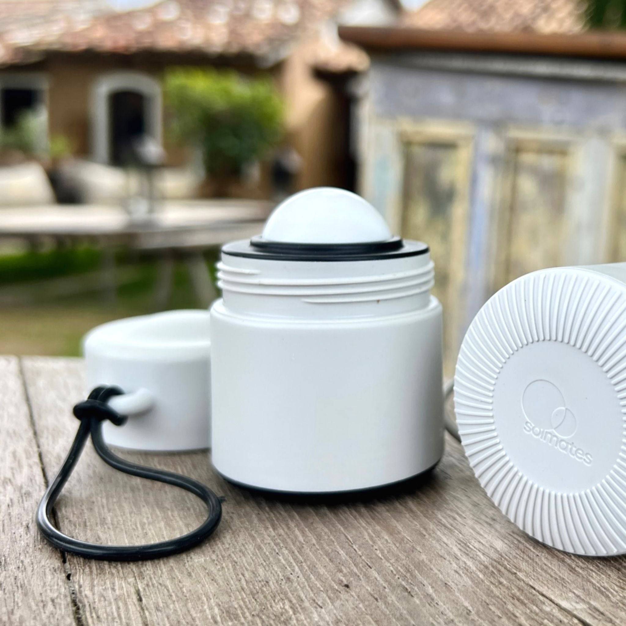 Grey and black refillable roll-on travel applicator with lid to the side on a wooden table