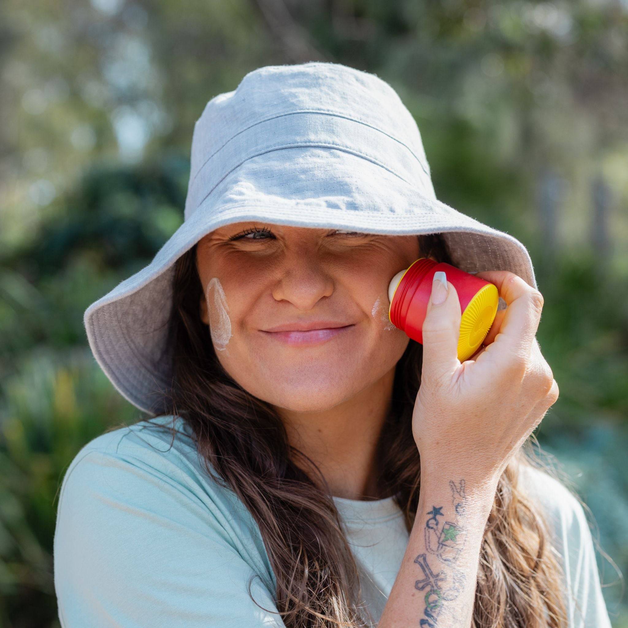 Red and yellow refillable roll-on travel applicator held to a woman's face