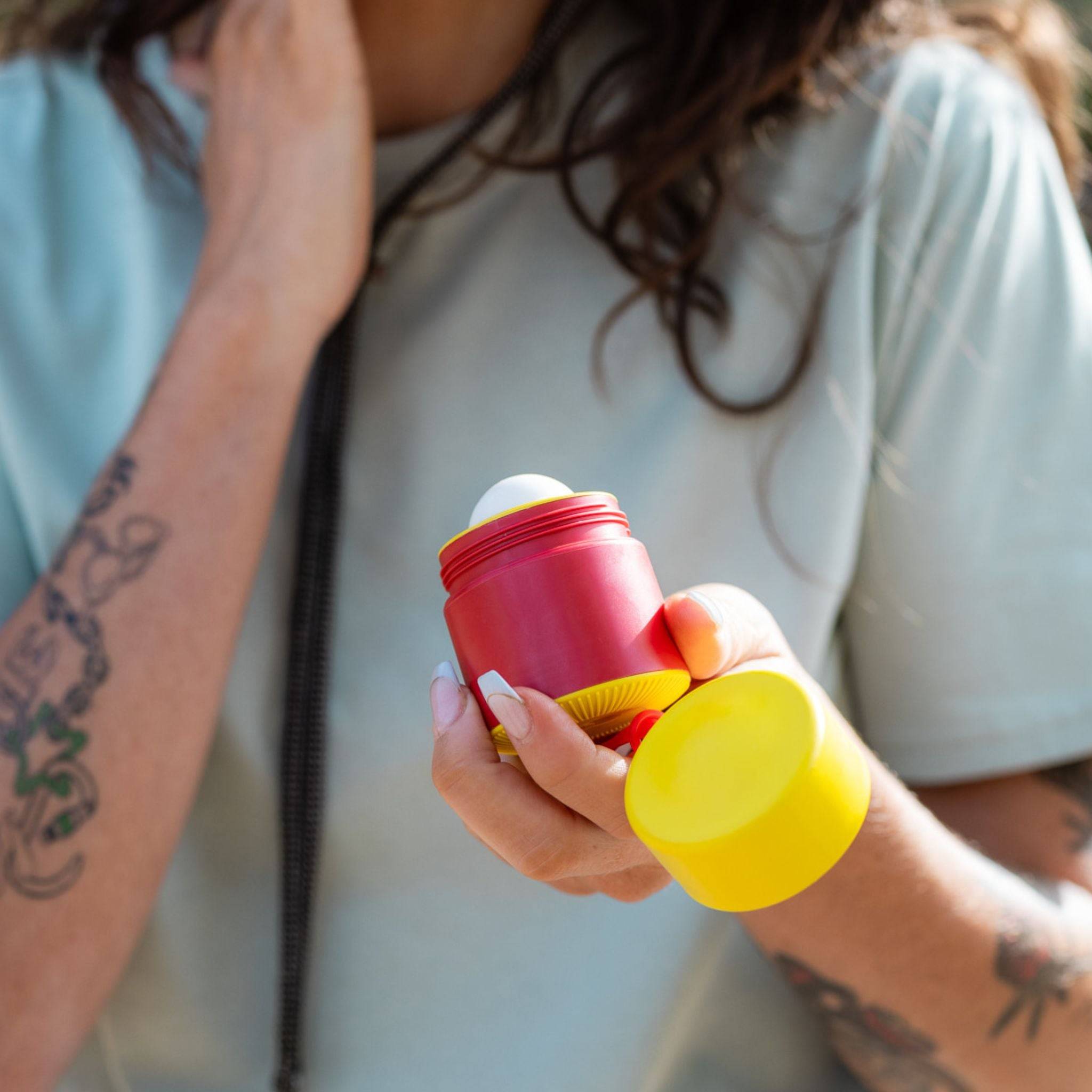 Red and yellow refillable roll-on travel applicator held in hands with the lid off