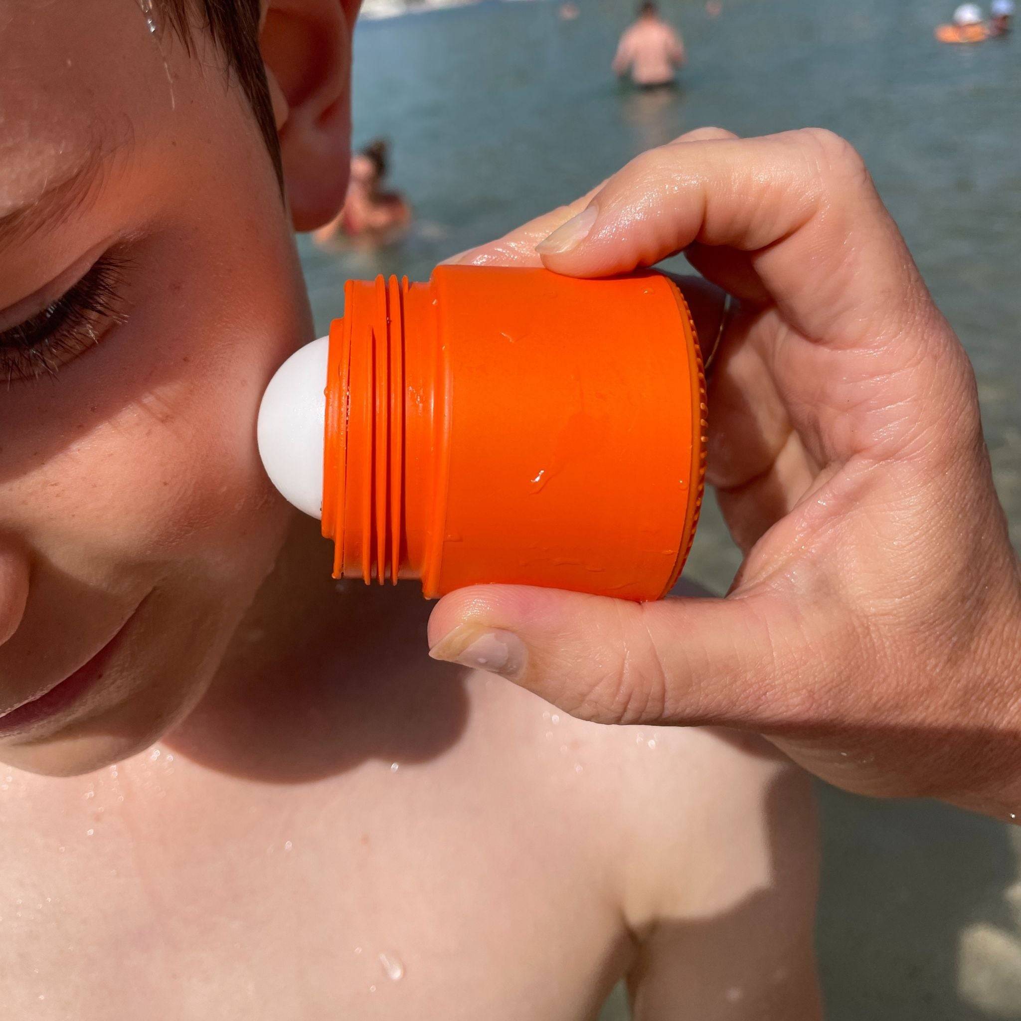 Orange refillable roll-on travel applicator applied to boy's face