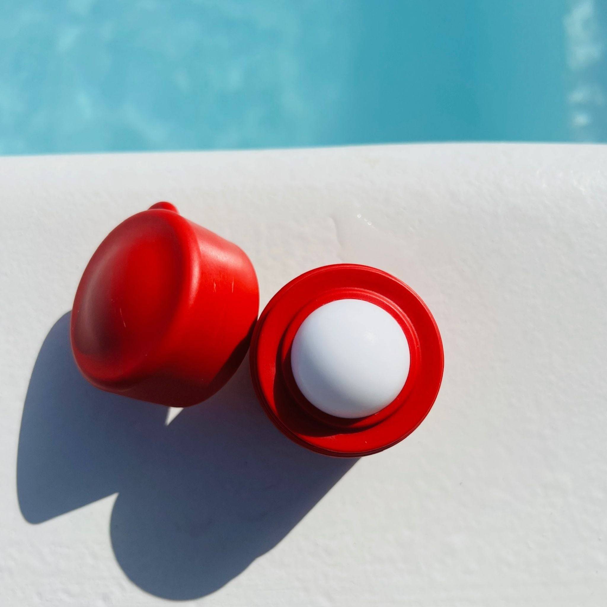 Top view of a red refillable roll-on travel applicator with lid balanced to the side