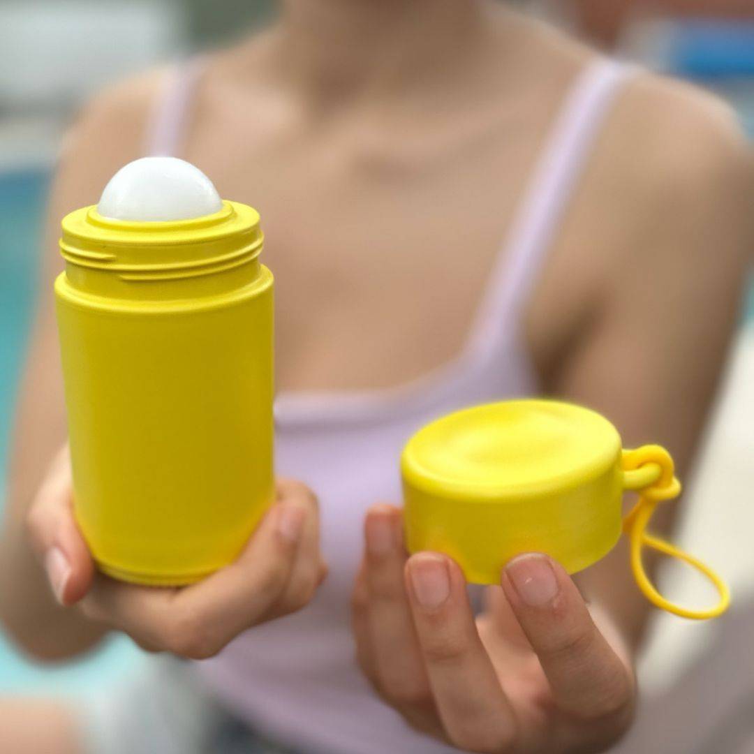 Yellow refillable roll-on travel applicator with lid held in hands of a woman