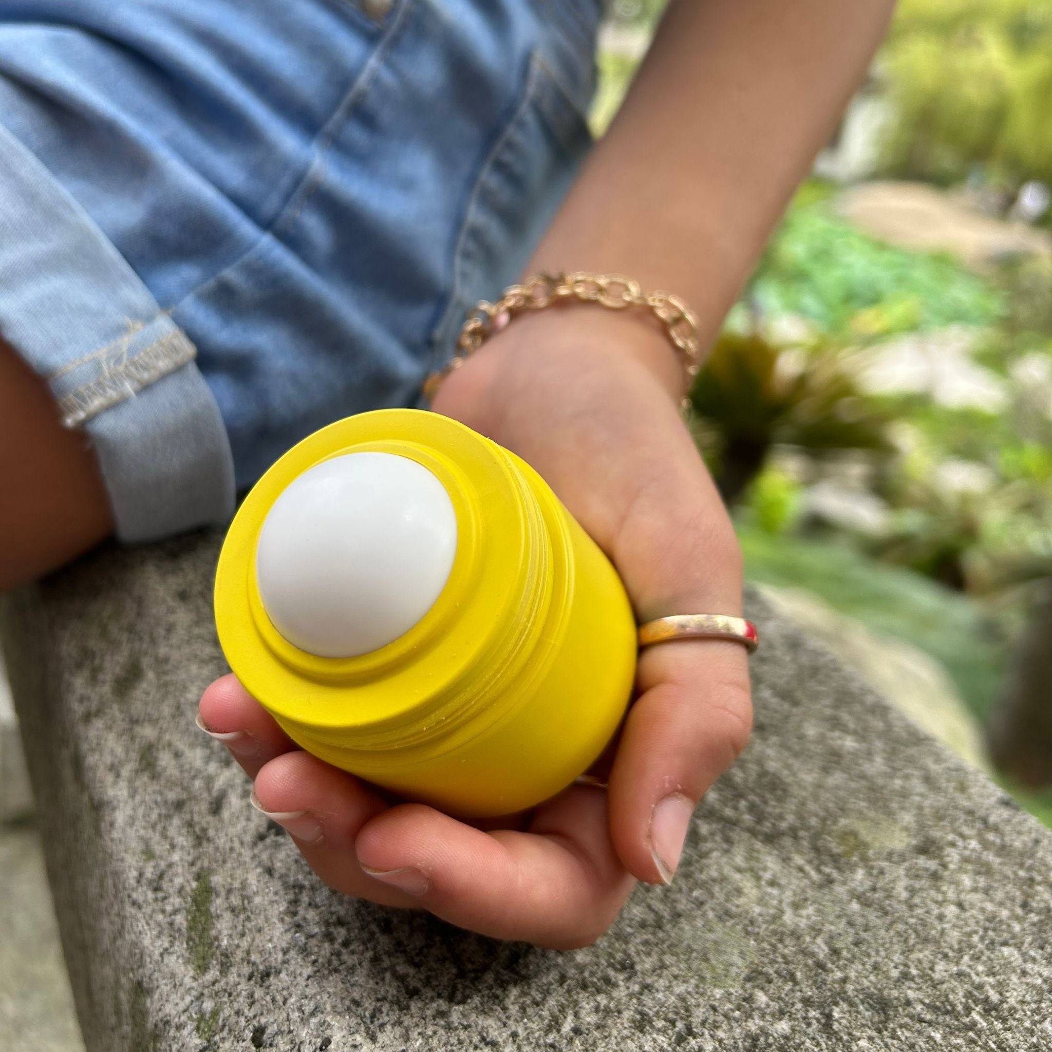 Yellow refillable roll-on travel applicator with lid off held in a hand