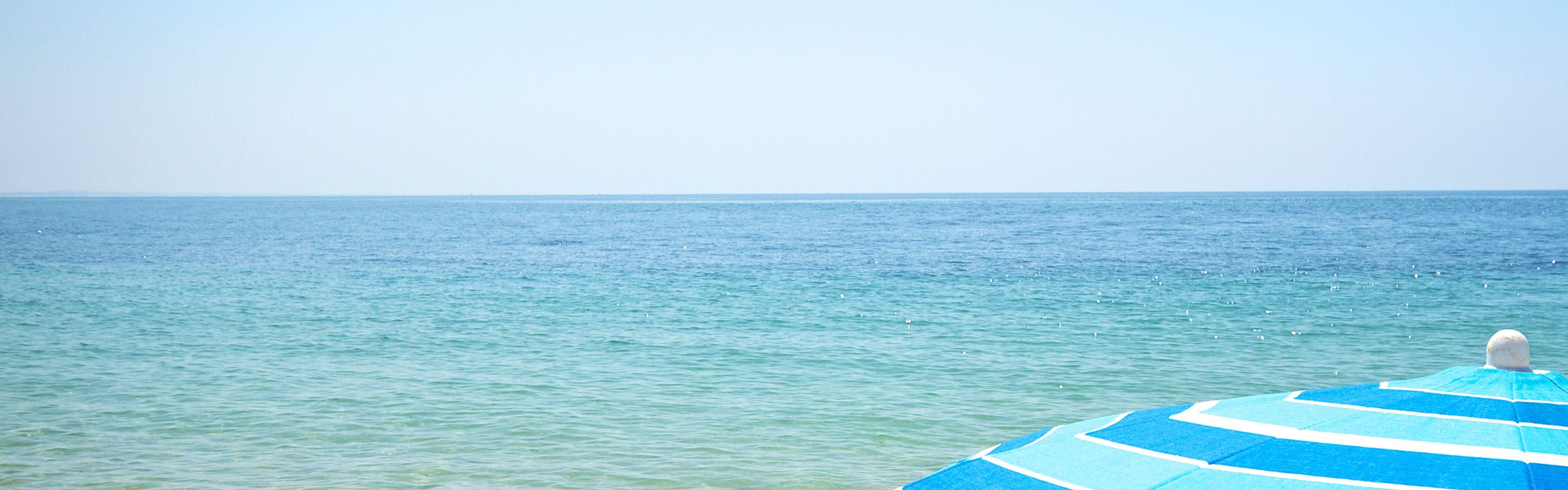 The beach in sunshine with a large beach umbrella in the corner