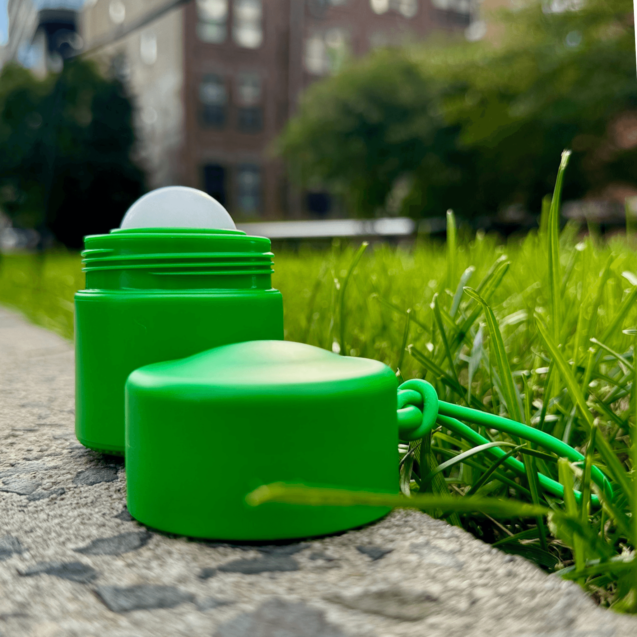 Green refillable roll-on travel applicator with lid to the side on a grey path next to grass